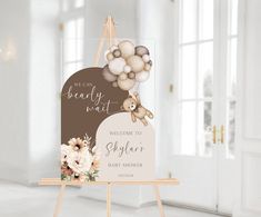 a baby shower sign with balloons and a teddy bear hanging from it's back