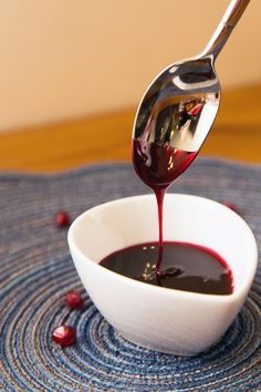 a spoon pouring red liquid into a white bowl on top of a blue place mat