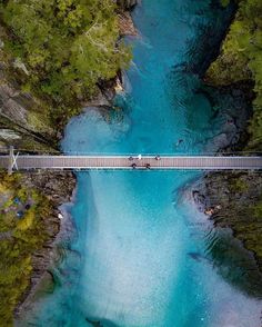 two people crossing a bridge over a river in the mountains, with blue water and green trees