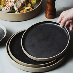 three black plates and one brown plate on a table with two people reaching for them