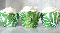 three green cupcakes with white frosting and leaf designs on them sitting on a marble surface