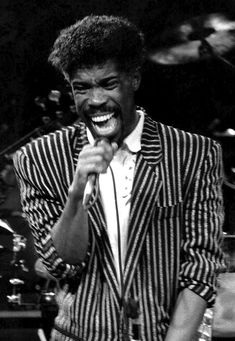 a black and white photo of a man singing into a microphone in front of drums