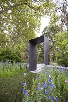 a sculpture in the middle of a garden with blue and purple flowers on it's side