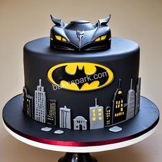 a batman themed birthday cake on a plate with city skylines and bat symbol in the middle