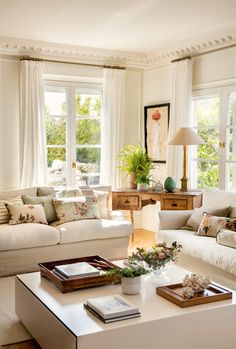 a living room filled with white furniture and lots of window sill space next to a coffee table