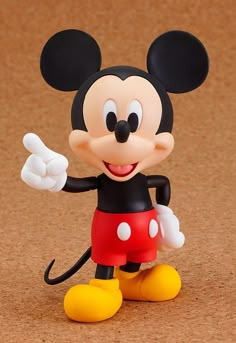 a mickey mouse figurine is posed on a brown surface with one hand in the air