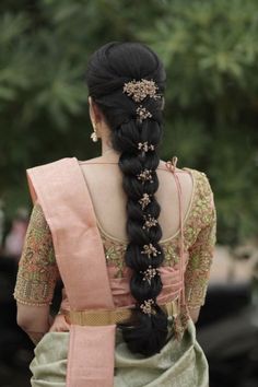 a woman with long black hair wearing a pink and green saree, braided into a ponytail