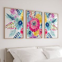 two paintings on the wall above a bed with white sheets and pillows, one is painted in bright colors