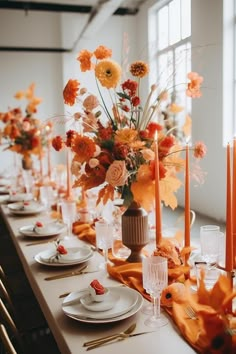 the table is set with orange and yellow flowers, candles, and white china plates