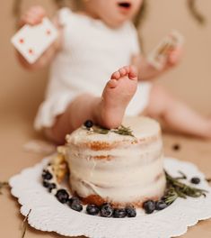 a baby is sitting on the floor next to a cake and holding a small piece of food