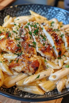 pasta with chicken and parmesan cheese in a black bowl on a wooden table