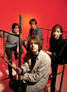 four people are posing for a photo in front of a red background with an old ladder