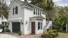 a white house with green shutters on the front and second story, surrounded by trees