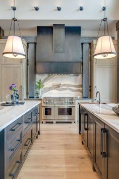 a large kitchen with an island, stove and oven in the center is surrounded by two pendant lights