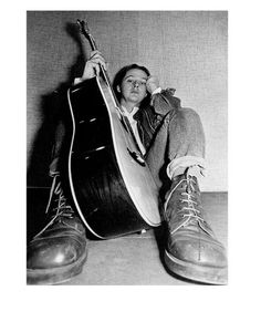 a black and white photo of a man sitting on the floor with a guitar in his hand