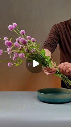 a woman arranging flowers on a table with a video screen showing how to arrange the stems