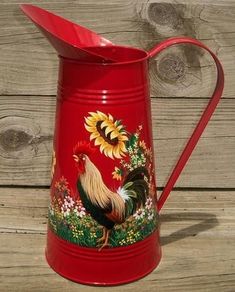 a red watering can with a rooster and sunflowers painted on the front side