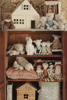 there are many stuffed animals on the shelves in this room and one is holding a doll house