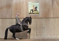 a man riding on the back of a black horse next to a wall and painting