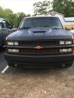 the front end of a black truck parked in a parking lot next to other cars