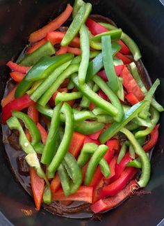 green peppers and red bell peppers cooking in a wok with brown sauce on the side