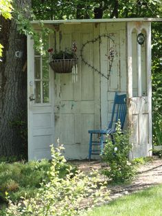 an outhouse in the woods with a blue chair and potted plant on it