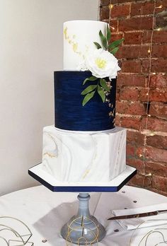 a three tiered white and blue wedding cake on top of a table with flowers