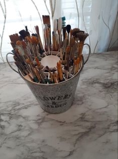 a bucket full of paint brushes sitting on top of a marble counter next to a window