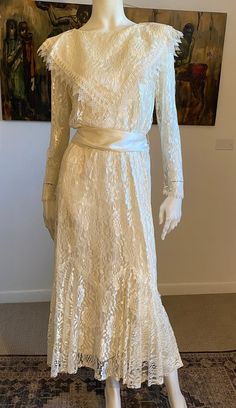 a mannequin wearing a white dress with long sleeves and a sash around the waist