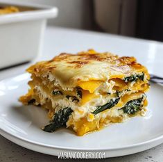 a white plate topped with lasagna covered in cheese and spinach