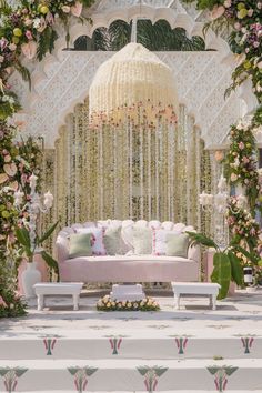 a white couch sitting under a chandelier covered in flowers and greenery on top of a stage