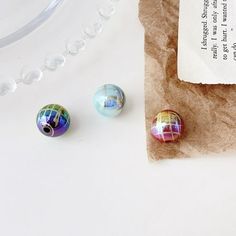 three colorful glass beads sitting on top of a piece of paper next to a bag