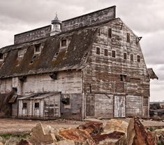 an old wooden barn sitting on top of a field next to some rocks and grass