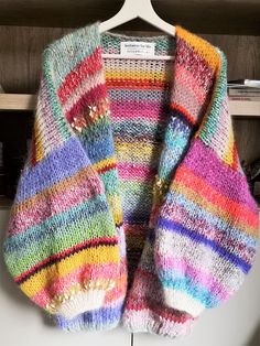 a multicolored sweater hanging on a white hanger in front of a bookcase