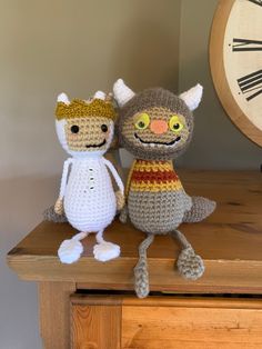 two crocheted cats sitting on top of a wooden table next to a clock