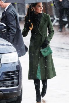 the woman is walking in the rain with an umbrella over her head and she is wearing a green coat