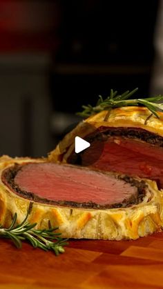 a piece of meat is cut in half on a cutting board with rosemary sprigs