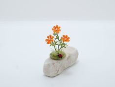 an orange flower sitting on top of a rock next to a ladybug figurine