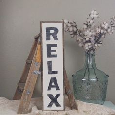 a wooden sign that says relax next to a vase with cotton flowers and ladders