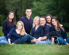 a group of people sitting on top of a lush green grass covered field in front of trees