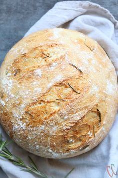 a round loaf of bread sitting on top of a white cloth next to a sprig of rosemary