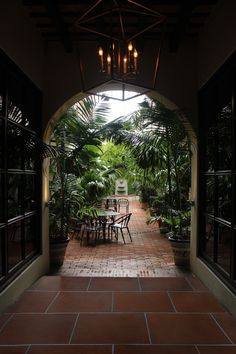 an archway leading to a dining area with tables and chairs in the center, surrounded by greenery