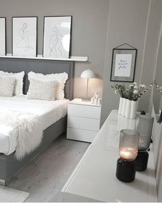 a white and gray bedroom with pictures on the wall above the bed, bedside table