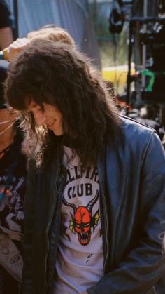 a man with long hair standing in front of a camera and looking at his cell phone