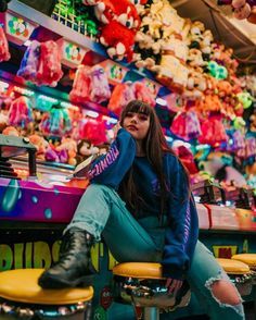 a woman sitting on top of two stools in front of a store filled with stuffed animals