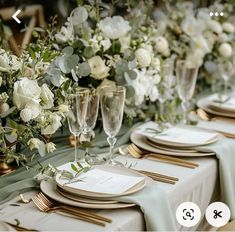 the table is set with white flowers and gold place settings