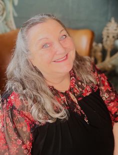 an older woman sitting in a chair smiling at the camera with grey hair and blue eyes