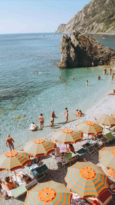 many people are on the beach with orange and blue umbrellas