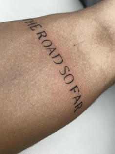 a person with a tattoo on their arm that says the road so far in cursive writing