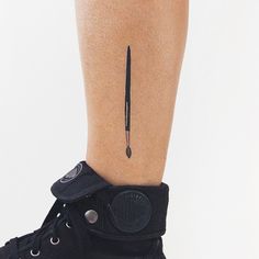 a tattoo on the leg of a person with black shoes and a pen sticking out of it